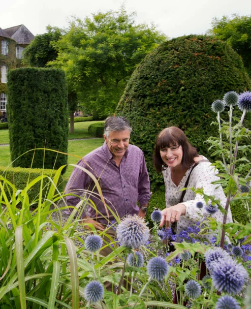 Smiling couple exploring a manicured hotel garden with trimmed hedges and purple globe thistles