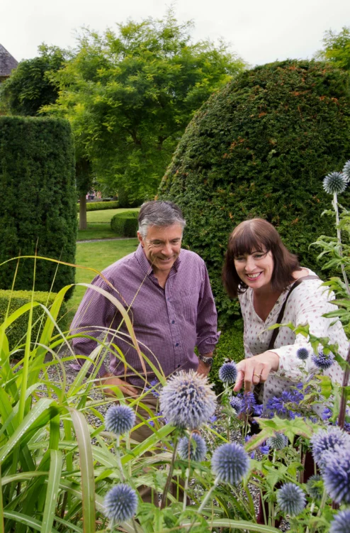 Smiling couple exploring a manicured hotel garden with trimmed hedges and purple globe thistles