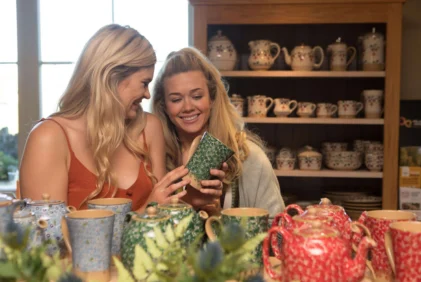 Two women smiling as they examine a patterned teacup in a cosy pottery shop, family-friendly stay setting