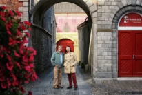 Mature couple strolling under a stone archway by Smithwick’s red doors, smiling together