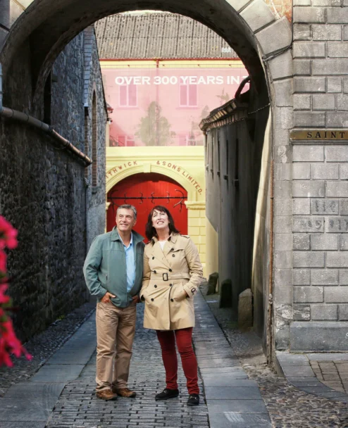 Mature couple strolling under a stone archway by Smithwick’s red doors, smiling together