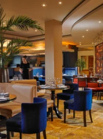 Family dining in a warm hotel restaurant, server setting wine at an elegant table with plants