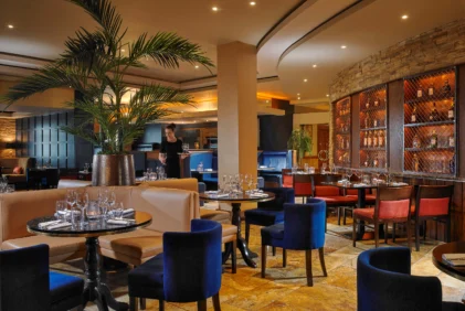 Family dining in a warm hotel restaurant, server setting wine at an elegant table with plants