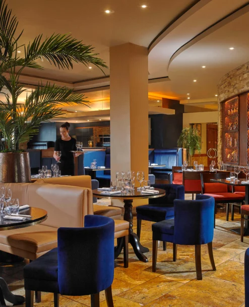 Family dining in a warm hotel restaurant, server setting wine at an elegant table with plants