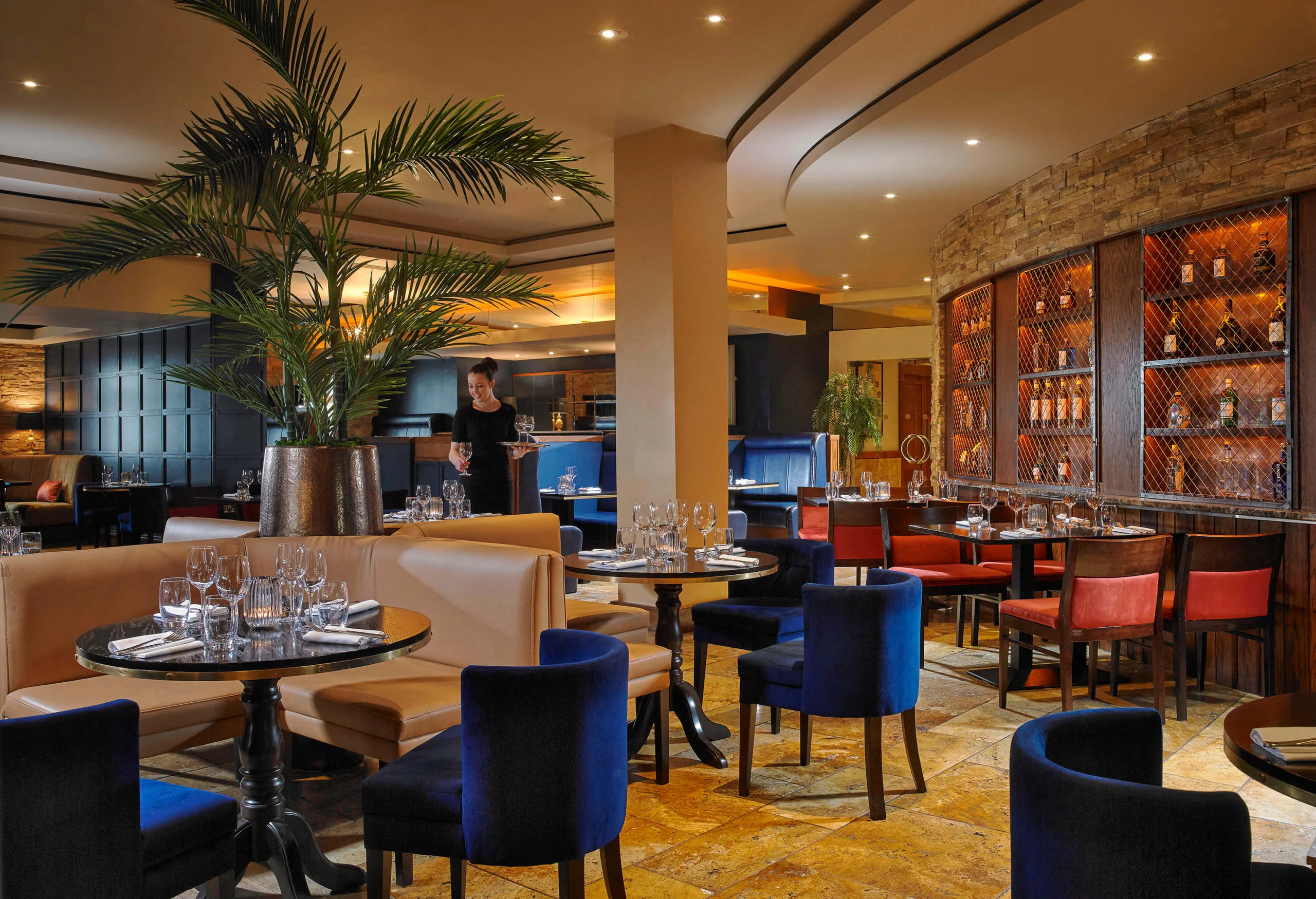 Family dining in a warm hotel restaurant, server setting wine at an elegant table with plants