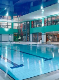 Family enjoying indoor hotel pool area with a parent and child walking by the water, turquoise décor (no visible text)