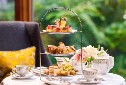 Three-tier afternoon tea with sandwiches, scones and pastries on a cosy hotel table, family setting (no visible text)