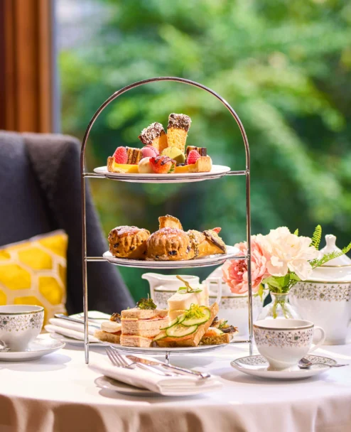 Three-tier afternoon tea with sandwiches, scones and pastries on a cosy hotel table, family setting (no visible text)