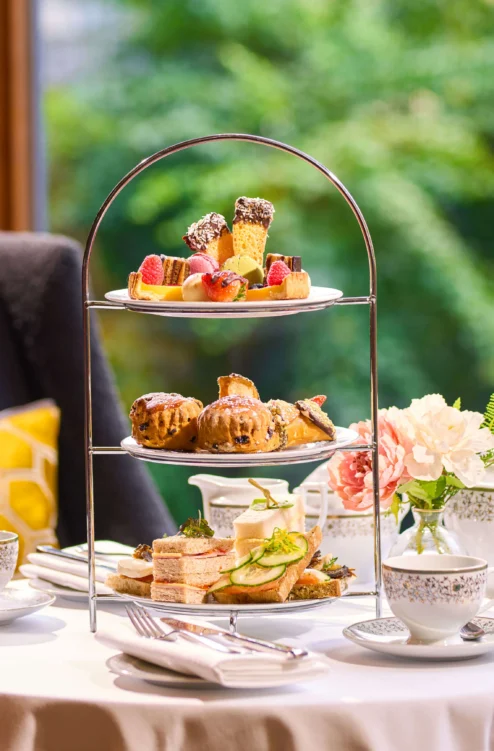 Three-tier afternoon tea with sandwiches, scones and pastries on a cosy hotel table, family setting (no visible text)
