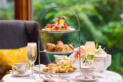 Three-tiered afternoon tea stand with sandwiches, scones and pastries by a window, cosy family setting