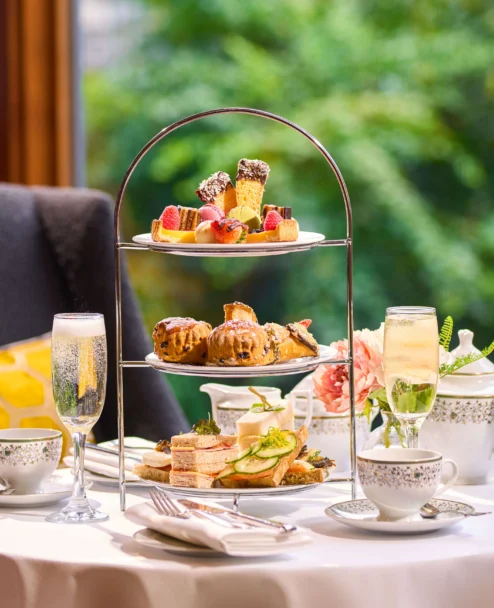 Three-tiered afternoon tea stand with sandwiches, scones and pastries by a window, cosy family setting