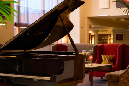 Grand piano in a warm hotel lounge with family seating, soft lamps and plants (no visible text)