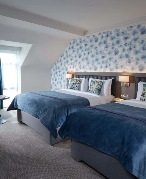 Cosy twin hotel room for a family or couple, two beds with blue throws, floral wallpaper, seating