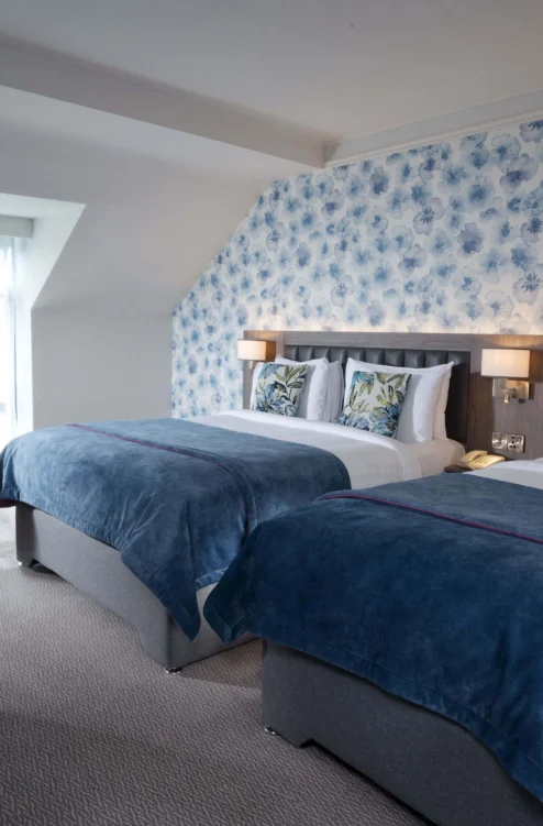 Cosy twin hotel room for a family or couple, two beds with blue throws, floral wallpaper, seating
