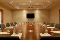 Spacious hotel meeting room with long wooden table, chairs, bottled water and notepads, warm lighting
