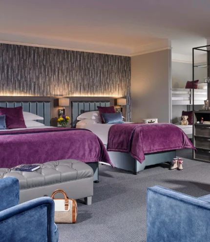 Spacious family hotel room with two double beds, purple throws, seating area and bunk for children