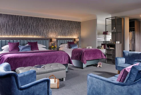 Spacious family hotel room with two double beds, purple throws, seating area and bunk for children