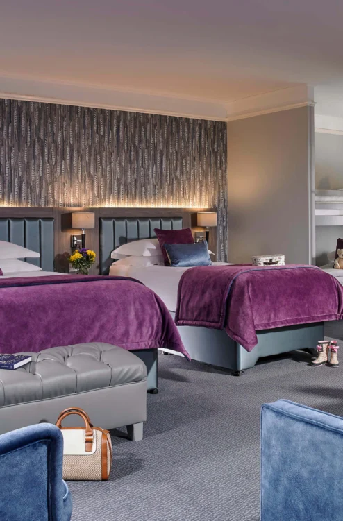 Spacious family hotel room with two double beds, purple throws, seating area and bunk for children
