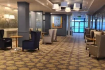Spacious hotel lounge with a family relaxing in armchairs by tables, warm lighting, patterned carpet (no visible text)
