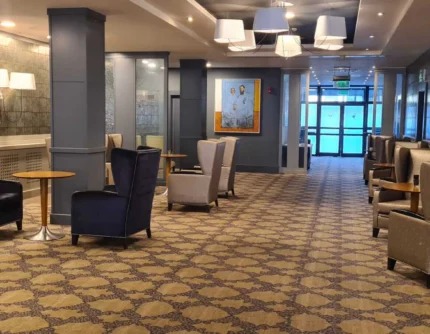 Spacious hotel lounge with a family relaxing in armchairs by tables, warm lighting, patterned carpet (no visible text)