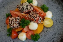 Fresh tomato and mozzarella salad with sesame‑crusted bites and parsley on a plate (no visible text)
