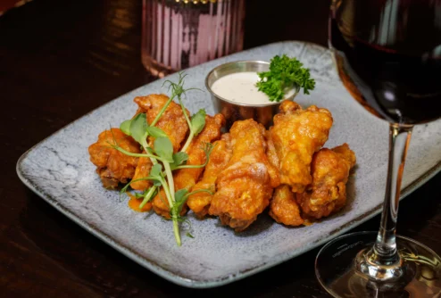 Crispy buffalo chicken wings with dipping sauce and microgreens on a stone plate, cosy dining setting
