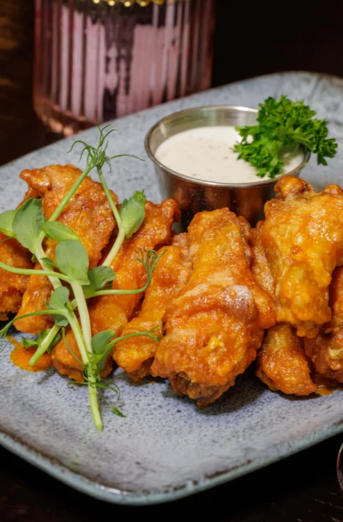 Crispy buffalo chicken wings with dipping sauce and microgreens on a stone plate, cosy dining setting