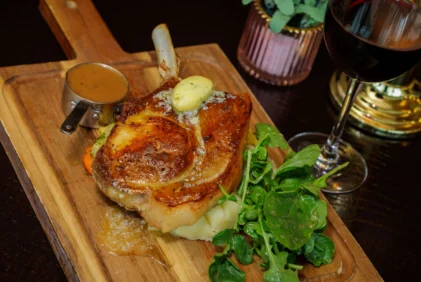 Roast pork chop with mashed potato, watercress, gravy and glass of red wine on wooden board