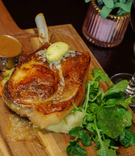 Roast pork chop with mashed potato, watercress, gravy and glass of red wine on wooden board
