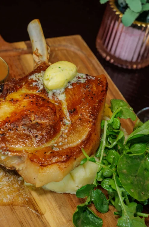 Roast pork chop with mashed potato, watercress, gravy and glass of red wine on wooden board