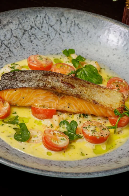 Pan-seared salmon with cherry tomatoes and creamy sauce, served with greens and a glass of white wine