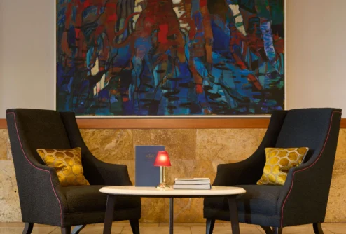 Cosy lounge seating for two with cushions, small table, lamp and abstract wall art in a hotel lobby