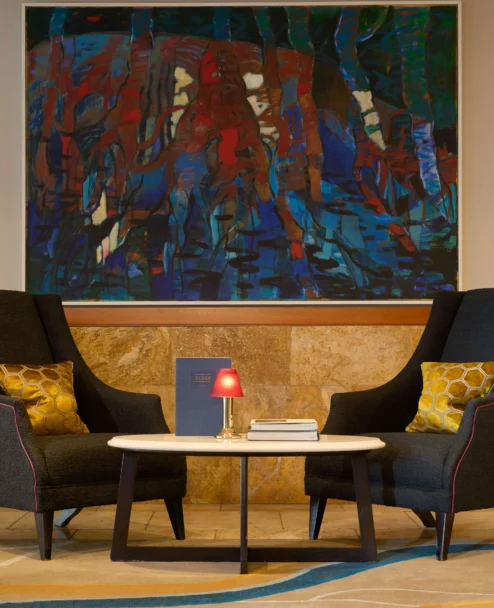 Cosy lounge seating for two with cushions, small table, lamp and abstract wall art in a hotel lobby