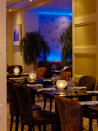 Warm hotel restaurant dining room with family-style table settings, soft candlelight and blue ambient lighting