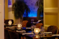 Warm hotel restaurant dining room with family-style table settings, soft candlelight and blue ambient lighting