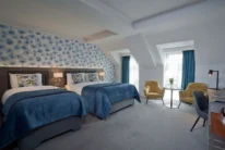 Family-friendly hotel room with two cosy twin beds, floral headboard, seating area and natural light