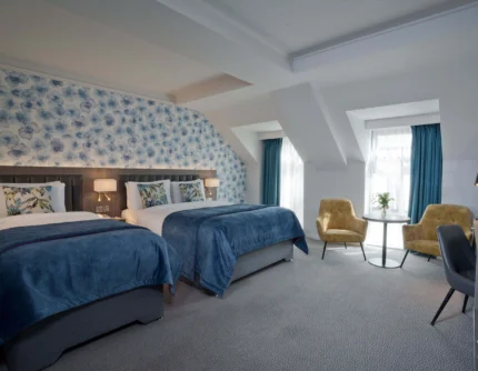 Family-friendly hotel room with two cosy twin beds, floral headboard, seating area and natural light