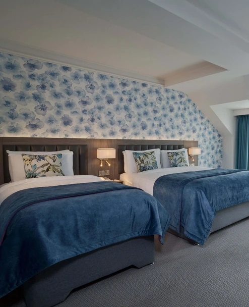 Family-friendly hotel room with two cosy twin beds, floral headboard, seating area and natural light