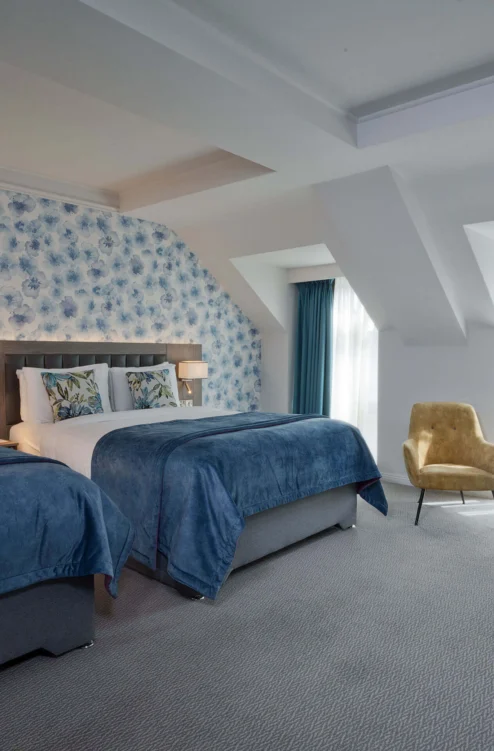 Family-friendly hotel room with two cosy twin beds, floral headboard, seating area and natural light