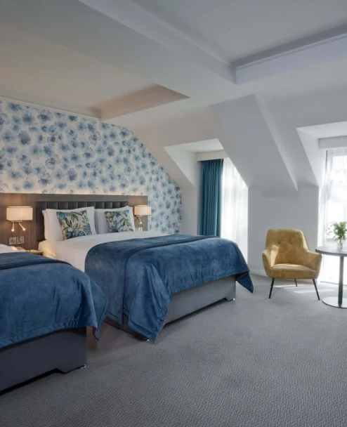 Cosy hotel twin room for families with floral feature wall, two beds, seating and natural light