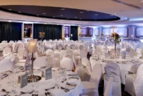 Elegant hotel banquet room set for a family celebration, round tables with white linens, candles and glassware