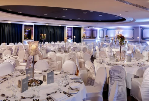 Elegant hotel banquet room set for a family celebration, round tables with white linens, candles and glassware