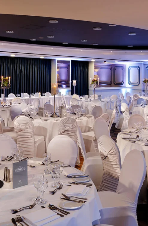 Elegant hotel banquet room set for a family celebration, round tables with white linens, candles and glassware
