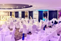 Elegant wedding reception in a hotel ballroom with family-style tables, cake and "LOVE" lights