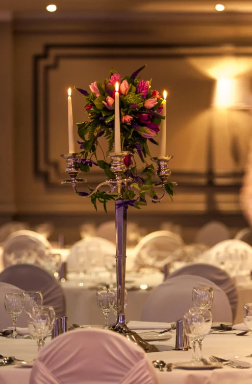 Elegant hotel banquet table with covered chairs, glassware and candlelit floral centrepiece, warm ambience