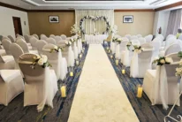 Intimate indoor wedding aisle with white chairs, floral decorations and heart archway