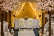 Intimate wedding scene with a couple’s chairs, floral aisle and warm fairy-lit backdrop, hotel venue