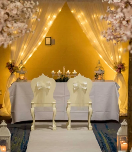 Intimate wedding scene with a couple’s chairs, floral aisle and warm fairy-lit backdrop, hotel venue