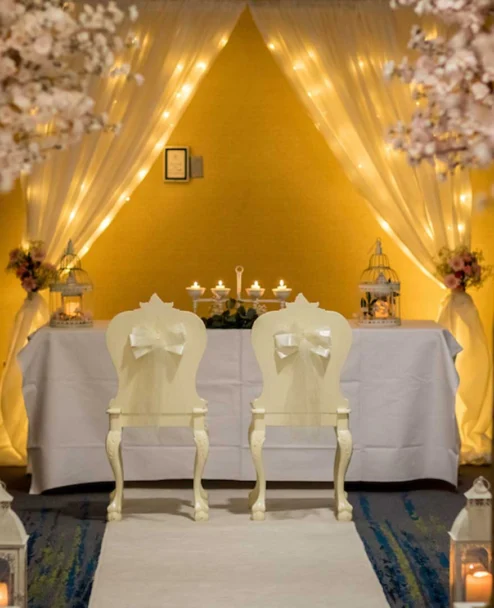 Intimate wedding scene with a couple’s chairs, floral aisle and warm fairy-lit backdrop, hotel venue