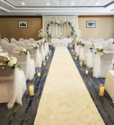 Intimate indoor wedding aisle with white chairs, floral decorations and heart archway